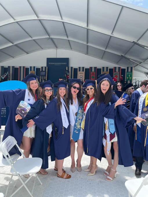 A group of people in graduation caps and gowns stand together smiling.