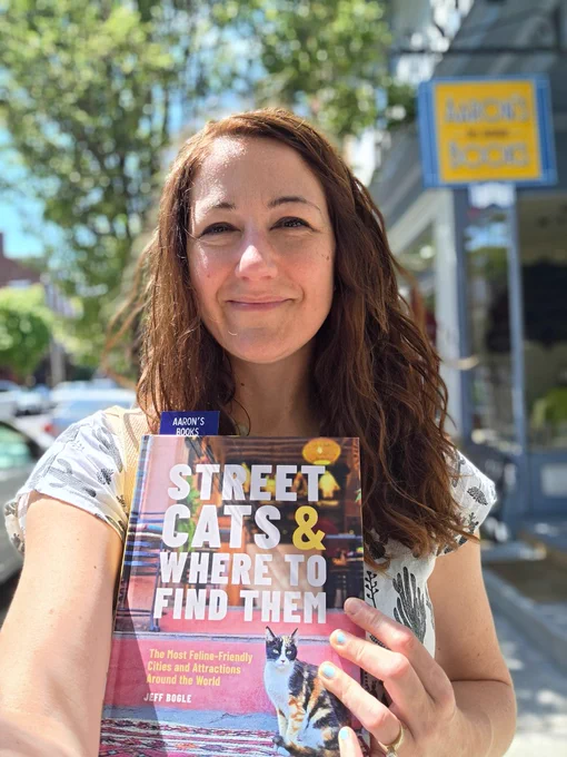 A woman standing in a town holding the book mentioned