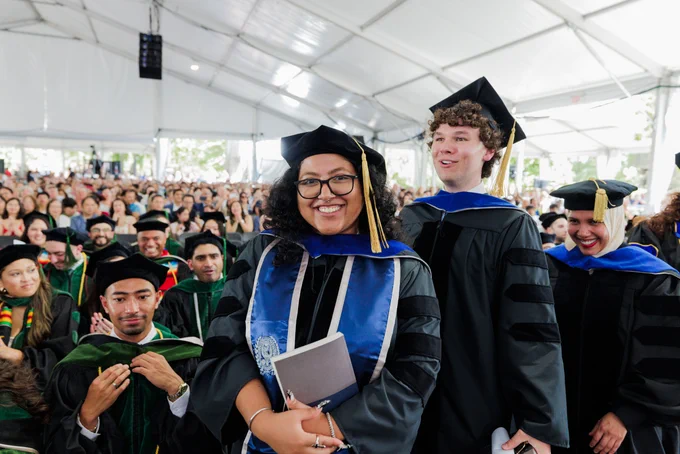 a woman with curly hair and glasses poses in grad regalia