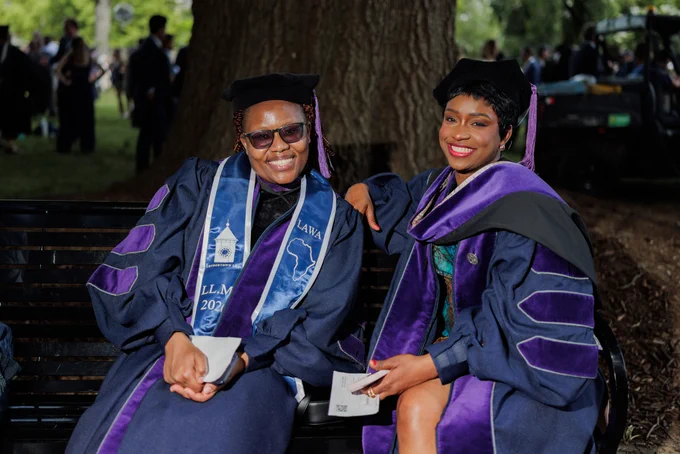 two women in purple law regalia sit on a bench