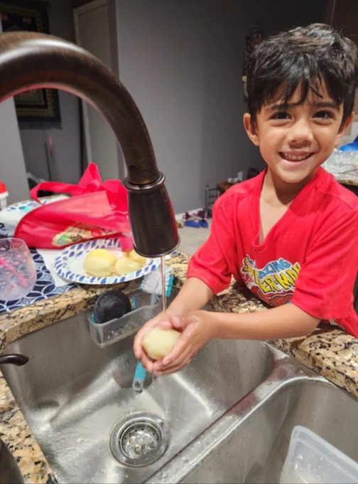 A child at the kitchen sink washing a potato.
