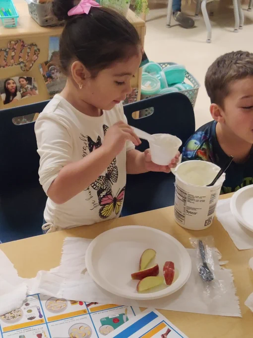 A child in a classroom scooping yogurt into a bowl. 
