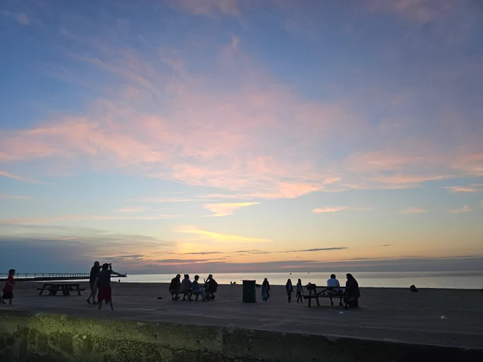 Cotton candy rainbow cloud skies above Lake Michigan with people in the foreground at the beach
