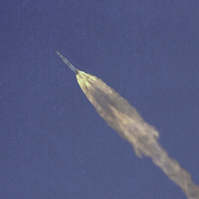 View from a distance of the Apollo 10 space vehicle high in Earth's atmosphere on May 18, 1969. Behind it is a trail of flame and exhaust.