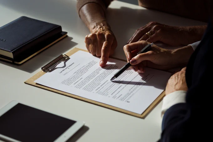 Two people reviewing and signing a document on a clipboard under natural light at a desk.