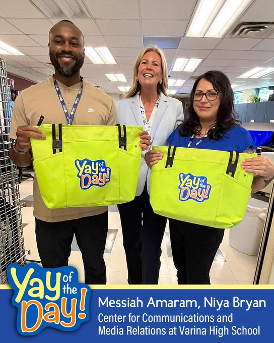 Three people holding tote bags with "Yay of the Day!" logo, smiling in an school setting.