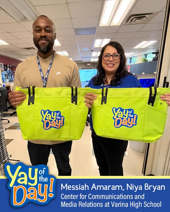 Two people holding "Yay of the Day!" bags, standing in what appears to be a school hallway or office.