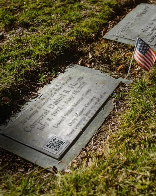 Titanium Memorial QR Tag With Custom Code And Details Mounted On Military Hero Memorial Displayed Outdoors With Small Flag