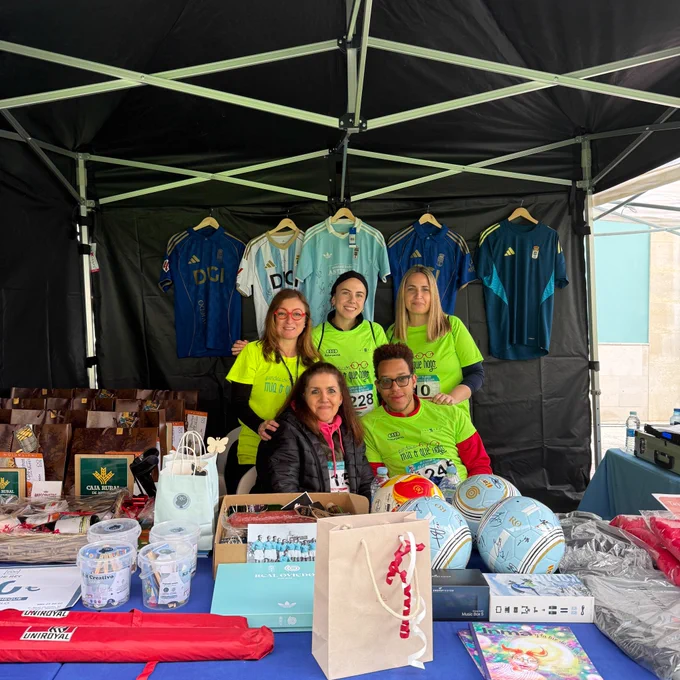 Representantes de Integra CEE posan en el interior de la carpa con merchandising y otros productos. Cuatro de las cinco personas llevan dorsales con el número de participación en la carrera y camisetas de color verde fosforito.