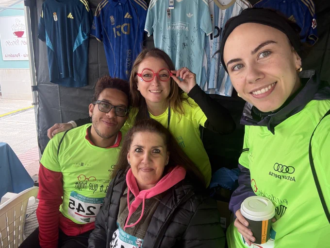 Un grupo de cuatro personas, todas ellas representantes de Integra CEE, se hacen un selfie en el interior de unos de los estands de la carrera. Dos de ellas llevan dorsales con el número de participante en la carrera. Al fondo se ven camisetas de fútbol oficiales de diferentes equipos con firmas de los jugadores.