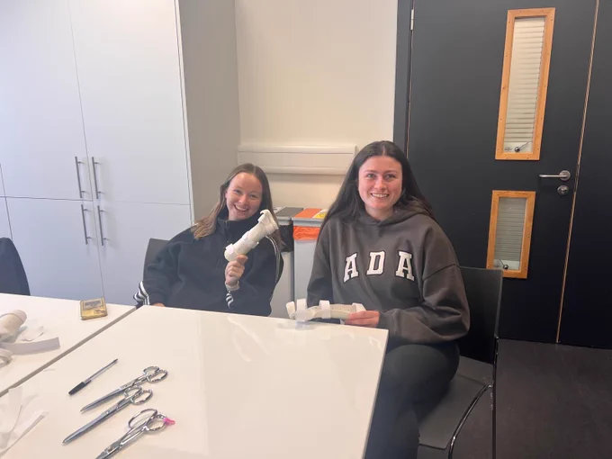Image shows two students smiling to camera and holding hand splints. 