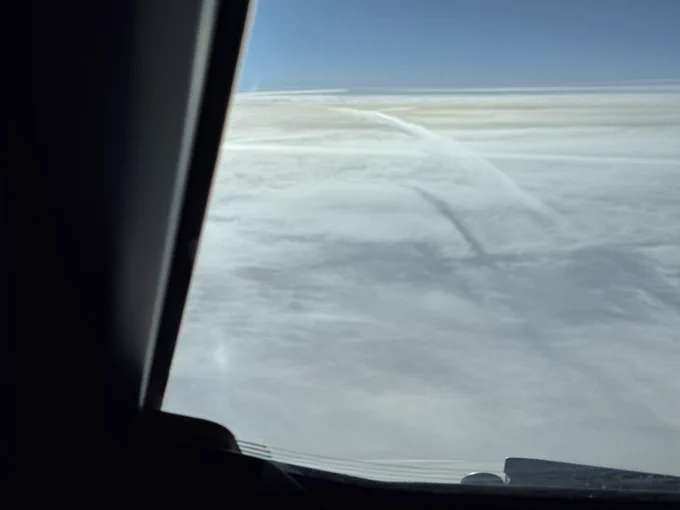 A contrail and its shadows on some clouds below. Curving away to the left.