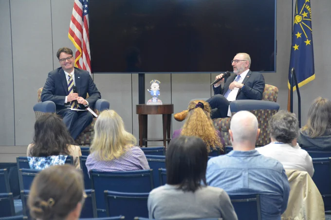 Photo of two people sitting on chairs in front of an audience. 