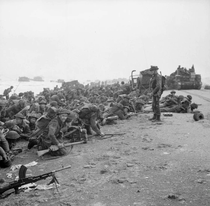 Commandos of 1st Special Service Brigade crouch on Queen beach in Normandy, Sword area, before moving inland, 6 June 1944.