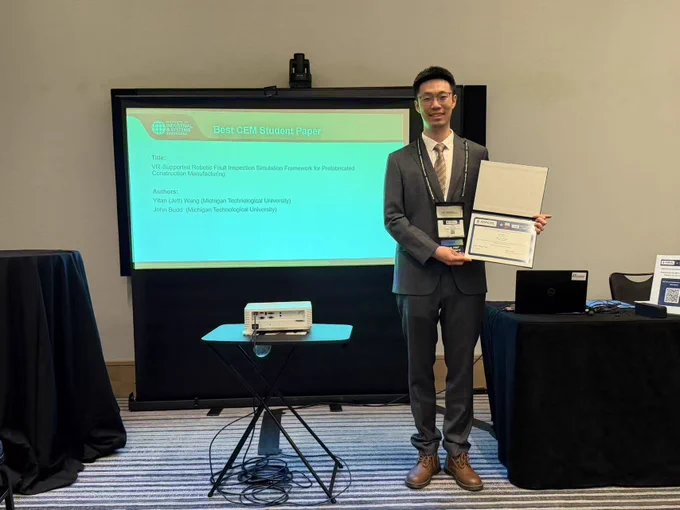 PhD student Yifan Wang stands in front of a presentation screen at the 2026 IISE Annual Conference & Expo, holding his Best CEM Student Paper award certificate and plaque. The presentation slide behind him displays the title of his award-winning paper, “VR-Supported Robotic Fault Inspection Simulation Framework for Prefabricated Construction Manufacturing.” Yifan is dressed in a gray suit and conference badge while smiling beside the display screen in the conference meeting room.