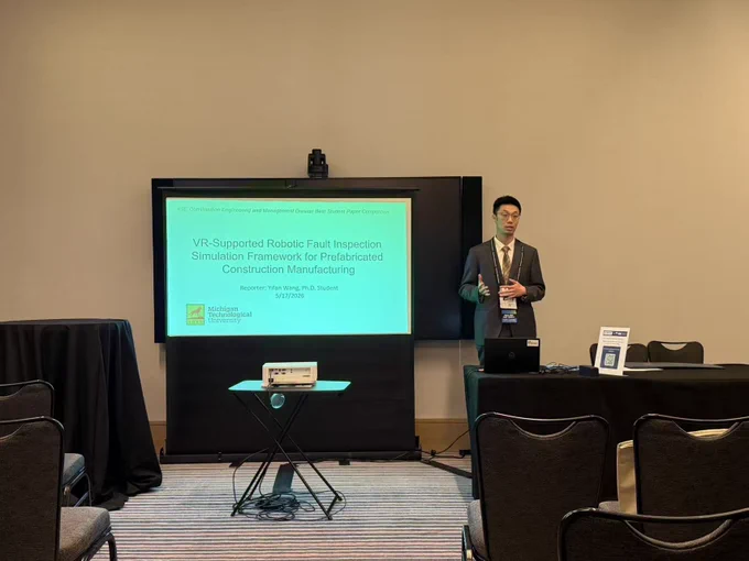 PhD student Yifan Wang presents his research during the Construction Engineering & Management Town Hall at the 2026 IISE Annual Conference & Expo. Standing beside a large presentation screen, Yifan gestures while discussing his award-winning paper titled “VR-Supported Robotic Fault Inspection Simulation Framework for Prefabricated Construction Manufacturing.” The conference room includes seating, presentation equipment, and Michigan Technological University branding on the slide.
