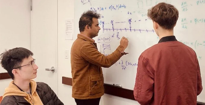 Dr. Sanket Rane writes on a whiteboard while members of his lab group watch and discuss.