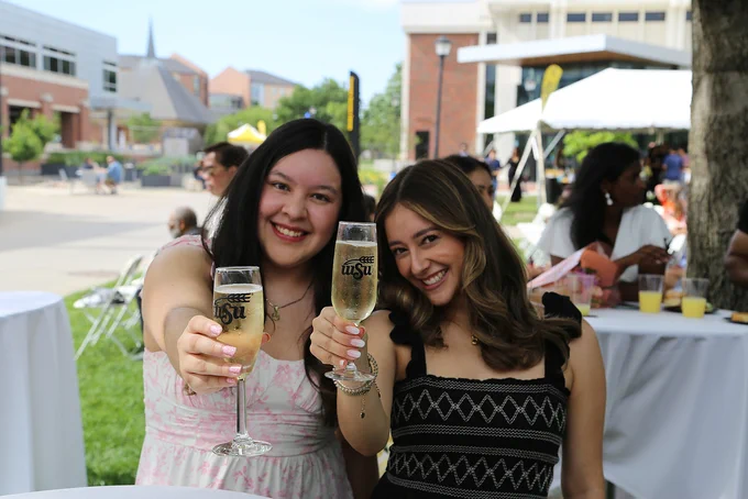 Two people smiling and holding glasses of champagne with a Wichita State University logo. 
