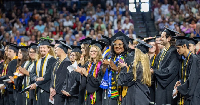 A group of people in graduation caps and gowns stand in rows during a ceremony. 