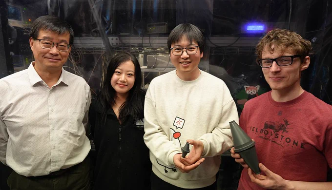 Four researchers, one older and three younger, pose in the lab holding models of a laser cavity.