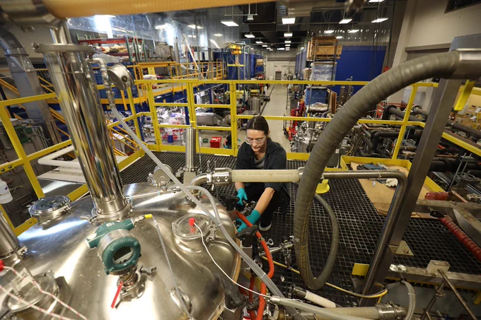 Technician wearing gloves working on complex industrial machinery inside a factory with yellow safety railings