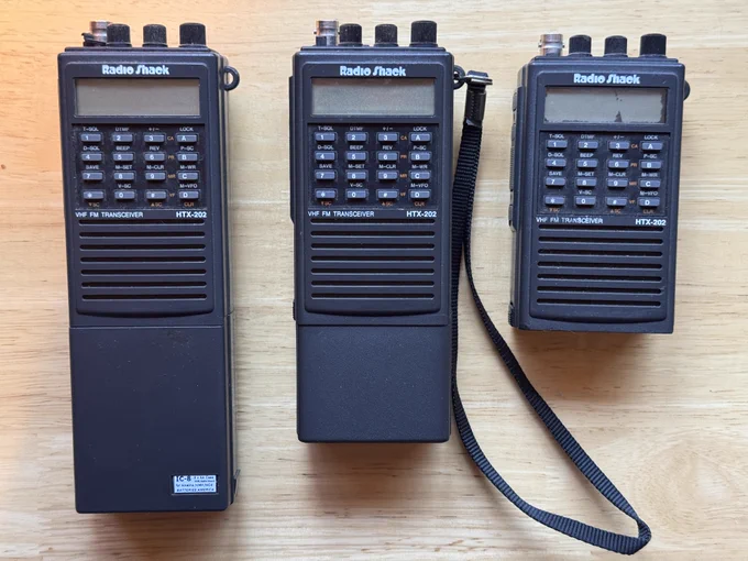 Three RadioShack HTX-202 handheld transceivers, from left to right: One I got at the 2024 Hamvention, one I got just a couple days ago at the 2026 Hamvention, and my original one from 1999 with a broken LCD screen.