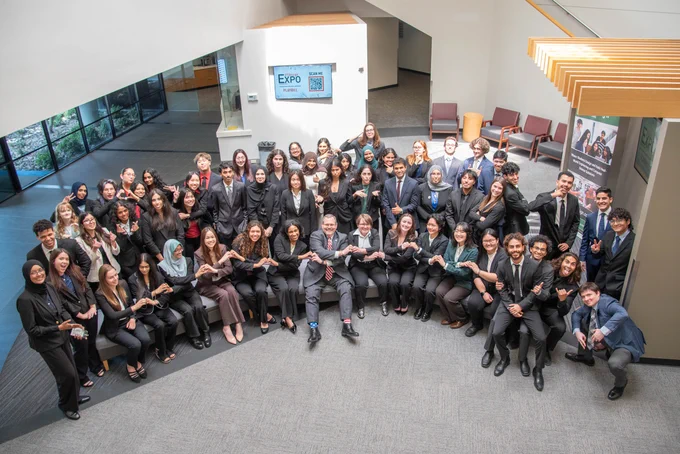 A large, diverse group of professionals in business attire gather in a spacious, modern lobby. They smile, conveying a sense of teamwork and achievement.