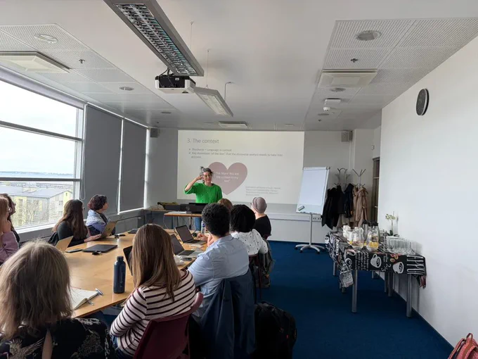 Audrey Alejandro teaching discourse analysis to a group of PhD students in front of a power point.