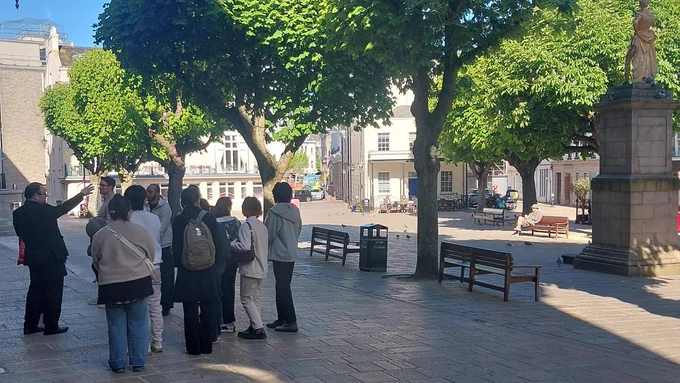 A group from King's College outside the Chamber in Royal Square. The statue of King George II is being pointed out to them.