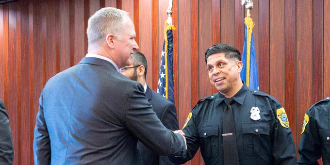 A person in a suit shakes hands with a uniformed police officer in a formal setting.