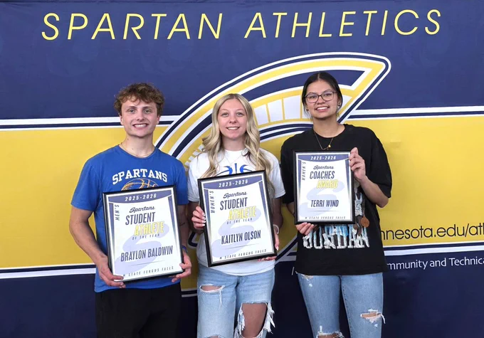 Three people are standing in front of a banner with "Spartan Athletics" and "Minnesota" visible. They are holding framed certificates. The certificates read "Spartan Student Athlete of the Year" for Braylon Baldwin, "Spartan Student Employee of the Year" for Kaitlyn Olson, and "Spartan Coaches Award" for Terri Vang.