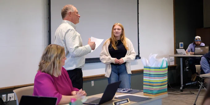 Man presenting a gift to a woman standing in front of a blank projection screen in a conference room.