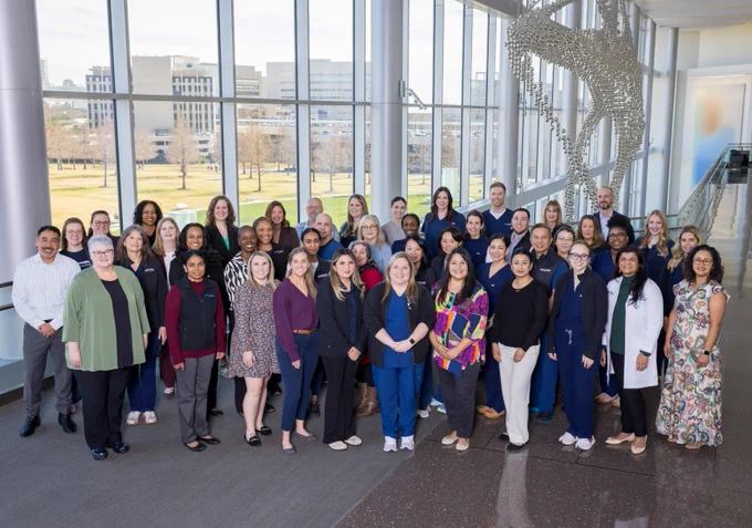 Group of Simmons Cancer Center nurses and employees posing together inside a building with large windows.