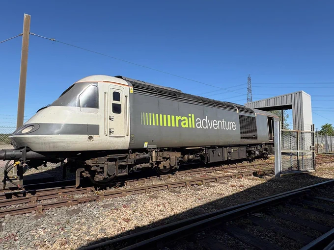 A train labeled "rail adventure" is on the tracks. The sky above is clear and blue.