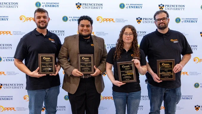Four individuals stand in front of a backdrop featuring the Princeton University and U.S. Department of Energy logos. Each person is holding a plaque. They are dressed in casual attire.