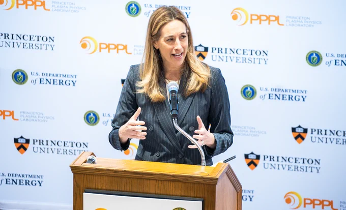 A person in a pinstripe suit speaks at a podium with a microphone. The background displays logos for Princeton University, PPPL, and the U.S. Department of Energy.