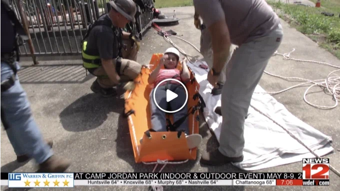 Rescue workers securing a person on an orange stretcher during an outdoor emergency drill. WDEF News 12 screen capture.