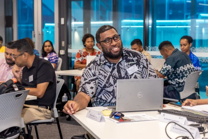 Participant smiling whilst seated working on a laptop during a group workshop in a modern office space.