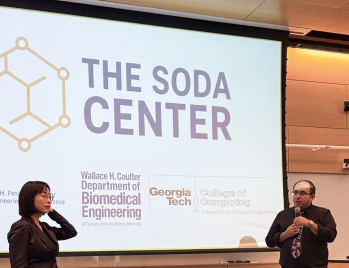 Two speakers stand in front of a projection screen displaying “THE SODA CENTER” alongside logos for Georgia Tech, the Coulter Department of Biomedical Engineering, and the College of Computing, during a seminar presentation.