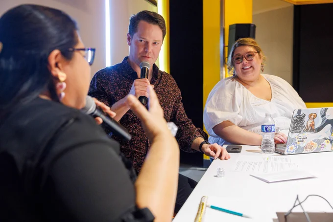 Photo of three people conversing during a podcast. Two people are holding microphones. 