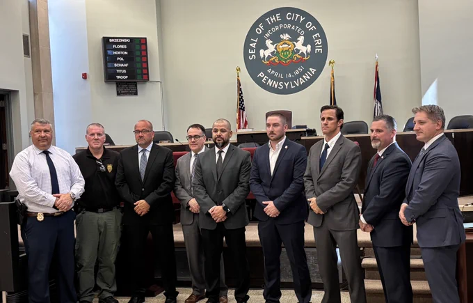 Image of nine law enforcement men standing in front of seal of Erie