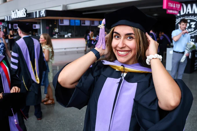 A student smiles at the camera as she adjusts her doctoral cap.