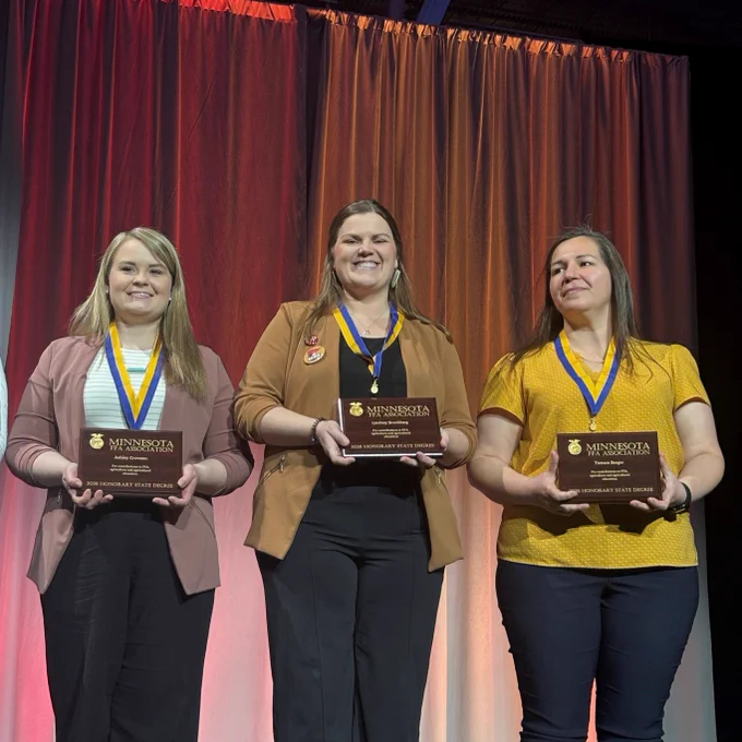  Lindsay Brockberg, center, stands on stage holding her award plaque and medallion with other honorees. Her plaque reads: Minnesota FFA Association. Lindsey Brockberg for contributions to FFA, agriculture and agriculture education. 2026 Honorary State Degree.