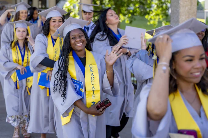 A RSC graduate is waving at the camera during the 2026 Commencement ceremony as students file in.