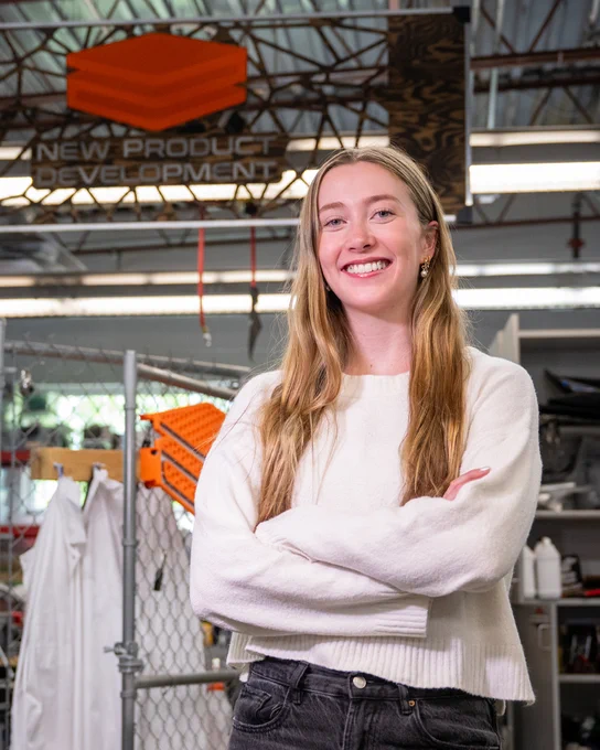 Boise State women's volleyball player Elle Cotton smiling in front of a New Product Development sign. 
