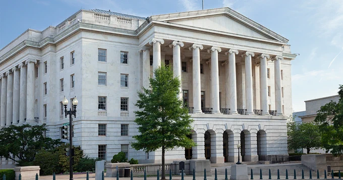 The image shows the Russell Senate Office Building in Washington, D.C. It is a neoclassical structure with tall columns and multiple stories. The building is surrounded by a few trees and a clear blue sky is visible.