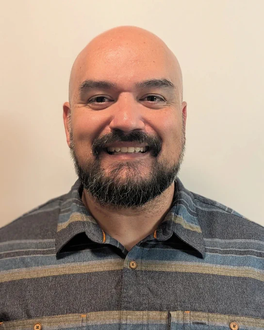 An individual smiling, they are wearing a striped shirt.