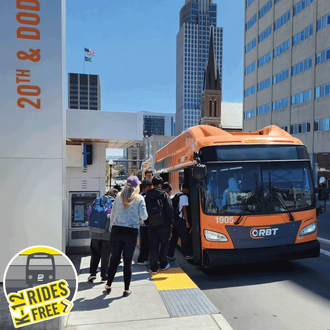 Students boarding an ORBT bus at 20th Street and Dodge Street in Omaha, Nebraska. Logo in bottom left reads, "K-12 rides free".