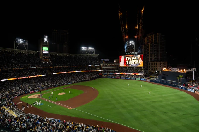 Overview of Petco Park after the Padres win. There are fireworks above the video board. There is text on the video board that says, "THAT'S THREE".