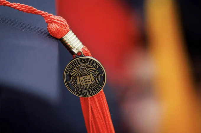 A Northeastern University graduation cap with a red tassel and a gold emblem featuring the university's name and seal.